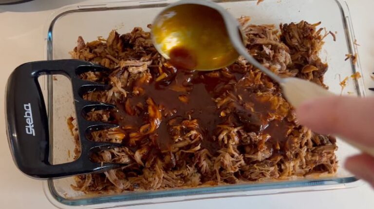 Pulled pork i glasskål, hvor BBQ-sovs hældes over det saftige kød.