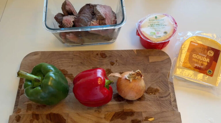 Ingredienser til Philly cheesesteak sandwich med oksekød, peberfrugt, løg, havarti og gouda klar til tilberedning.
