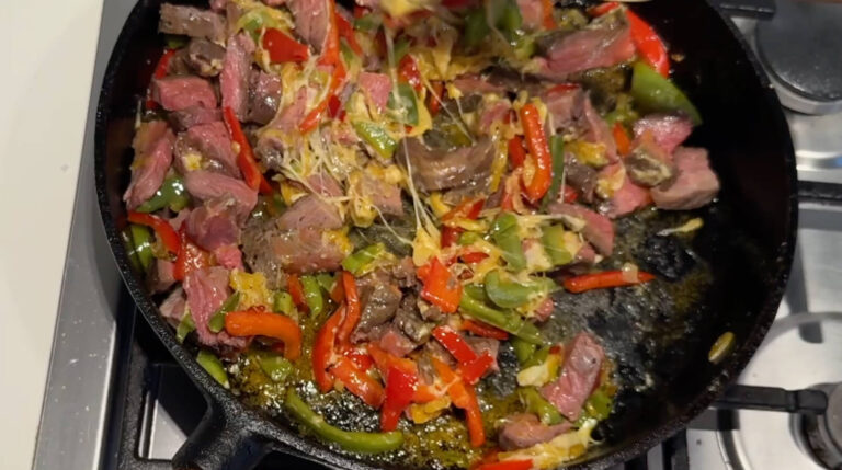 Oksekød tilsættes til panden med ost, løg og peberfrugt til en Philly cheesesteak sandwich.