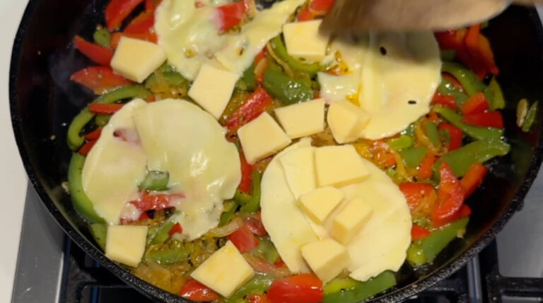 Havarti og gouda tilsættes til de stegte grøntsager for at lave cremet fyld til Philly cheesesteak sandwich.