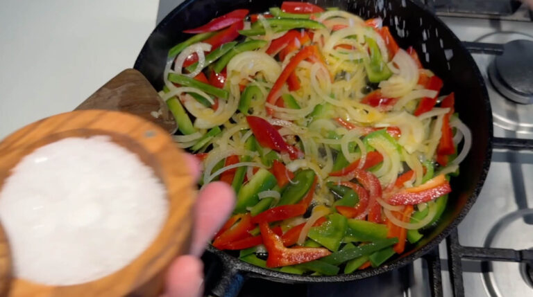 Salt drysses over stegte peberfrugter og løg på panden.