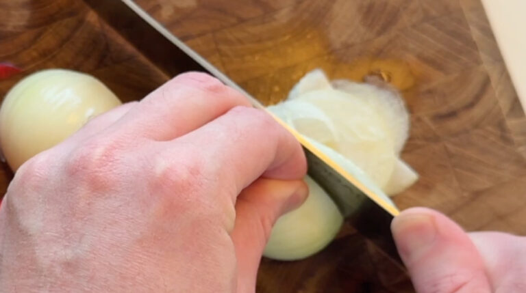 Løg skæres i tynde skiver på et skærebræt til en Philly cheesesteak sandwich.